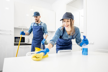 Man and woman as a professional cleaners in uniform washing floor and wiping furniture in the white...