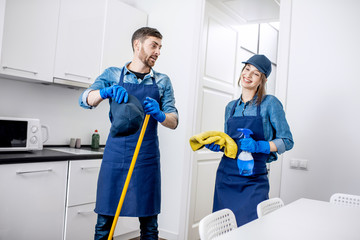 Portrait of a tired couple standing as a professional cleaners in uniform during the break in the kitchen