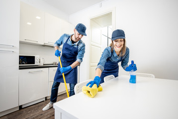 Man and woman as a professional cleaners in uniform washing floor and wiping furniture in the white...