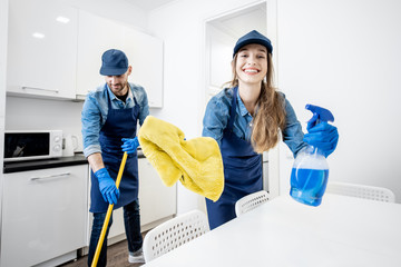 Funny portrait of a man and woman as aprofessional cleaner with cleaning tools in the white...