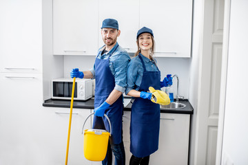 Portrait of a couple as a professional cleaners in uniform standing together with cleaning tools...