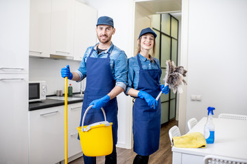 Portrait of a couple as a professional cleaners in uniform standing together with cleaning tools...