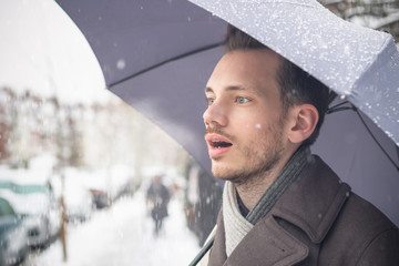 Handsome young man with umbrella breathing warm air in winter snow