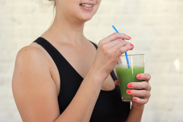 Sportswoman after fitness is holding green smoothie and drinking it