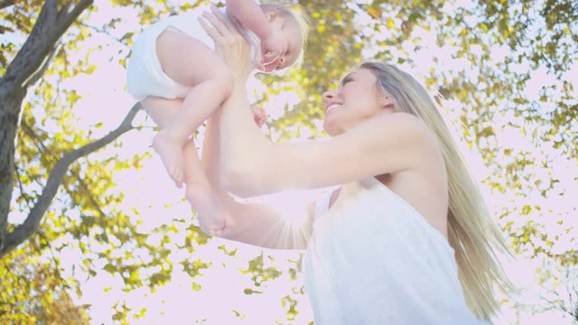 Beautiful young blonde mother bouncing her young baby boy in her arms outdoors 