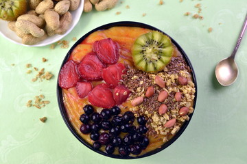 Breakfast with muesli, acai blueberry smoothie and kiwi, fruits on green background. Healthy food concept. Flat lay, top vie