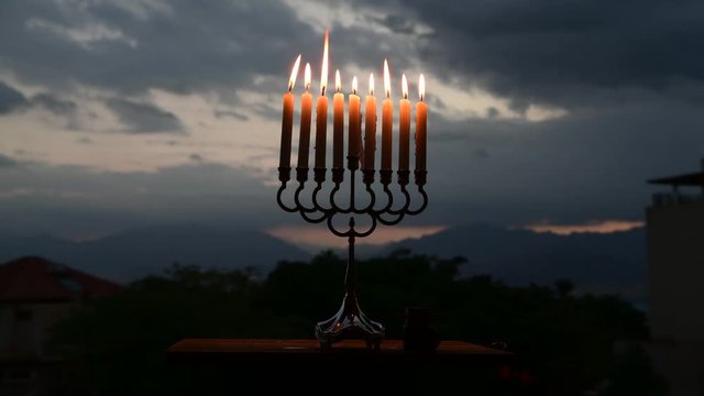 Menorah with burning candles is traditional symbol for Hebrew Holidays and celebration of Hanukkah. Background of night or dawn sky, selective focus on menorah