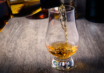 Pouring single malt scotch whisky into whisky glass on wooden table - 236580501