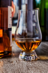 Whisky glass with single malt scotch on wooden table and scotch bottles on the background