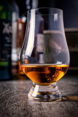 Whisky glass with single malt scotch on wooden table and scotch bottles on the background