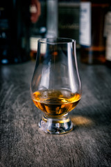 Whisky glass with single malt scotch on wooden table and scotch bottles on the background