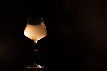 Burgundy crystal transparent red wine glass fully filled with white thick smoke, isolated close up on a black background in studio. Wine tasting concept