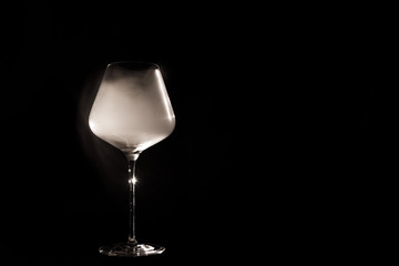 Burgundy crystal transparent red wine glass fully filled with white thick smoke, isolated close up on black background in the studio. Chemical party concept