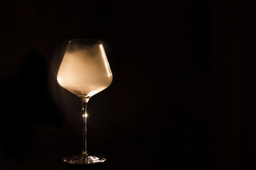 Burgundy crystal transparent red wine glass fully filled with white thick smoke, isolated close-up on a black background in the studio. The concept of  fun party and corporate chemistry lab
