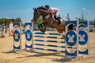 Girl riding her horse and jumping over the colorful obstacle during competition