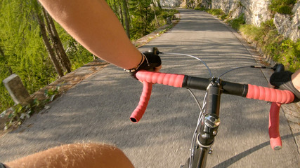 Naklejka premium POV: Pedalling a road bicycle up a steep asphalt road in the sunny mountains.