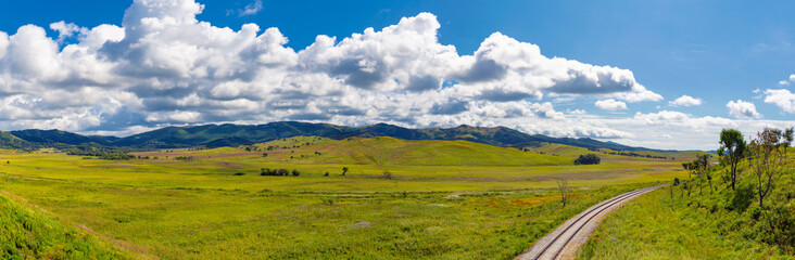 Fototapeta premium Panorama of green field and hills and a railroad on a cloudy day in early fall season