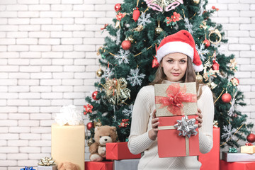 Young and beautiful caucasian woman holding gift boxes.There is big decorated christmas tree in background.