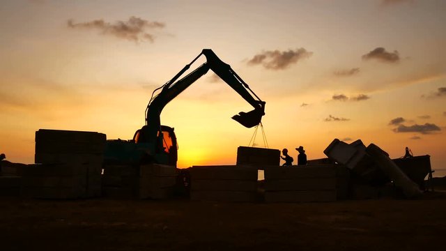 Construction Video At construction site The silhouette excavator is digging ground and lifting a large mortar, with engineering and construction workers to help with colorful sunset .