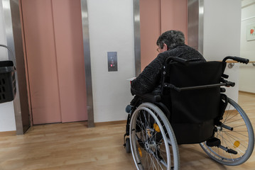 Alte Frau im Rollstuhl vor Aufzug