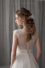 A beautiful bride is standing with her back. Lace dress. Head in profile. Wedding hairstyle and makeup. Decorations in hair.