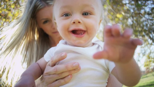 Portrait if beautiful young blonde Caucasian mother bouncing her young baby son in her arms outdoors 