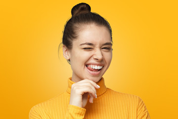 Beautiful girl in bright yellow polo neck sweater. smiling and winking to camera