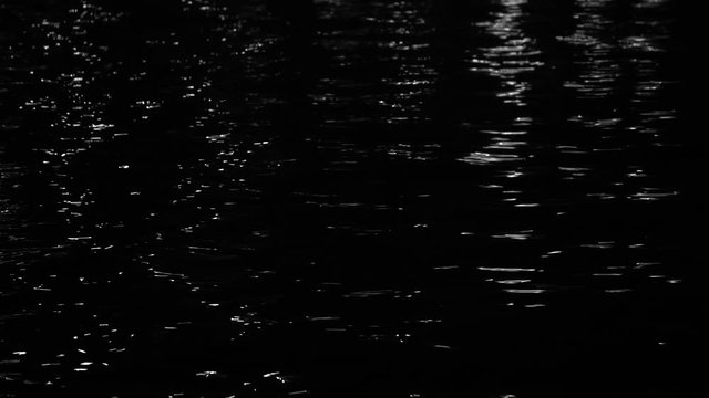 Black night sea water background with light reflections on calm surface. Real time 4k video footage.