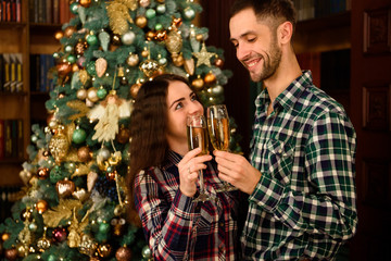 Beautiful young couple is holding glasses of champagne and smiling while celebrating at home