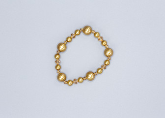 gold colored and variously sized beads bracelet on gray background