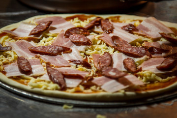 Raw pizza with sausage, bacon and cheese
