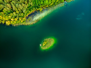 Aerial top down view of small island. Birds eye view of beautiful green waters of lake Gela surrounded by pine forests, near Vilnius city, Lithuania.