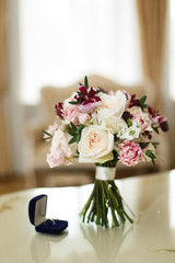  Bridal bouquet of white roses and burgundy orchids on the table and wedding rings close up 