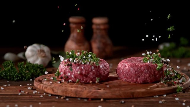Super slowmotion footage of strewing salt and herbs at fresh raw beef meat burger, 1000fps, 4K