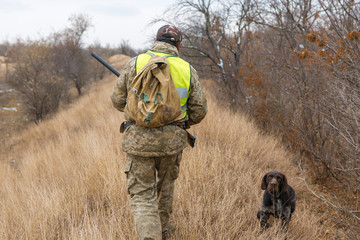 Hunter with a gun and a dog go on the first snow in the steppe, Hunting pheasant in a reflective...