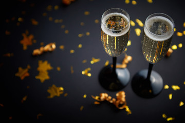 Two glasses full of sparkling champagne wine with golden decoration of confetti and serpentines on...