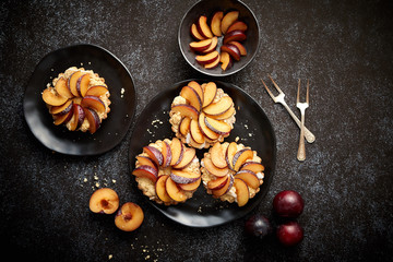 Delicious homemade mini tarts with fresh sliced plum fruit. Sprinkled with icing sugar. Placed on...
