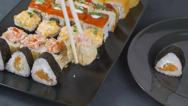 Top view on traditional japanese empty square black slate plate framed with sushi, ginger, soy, wasabi bowls, green leaves and chopsticks on rustic grey backround