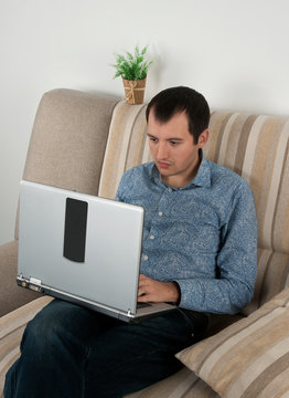 young man holding a laptop, working on the couch