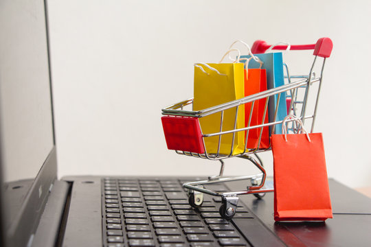 Colorful paper shopping bags in a trolley or shopping cart on laptop,E-commerce concept.