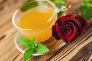 Glass cup with green tea and mint near red rose on sprig on old wooden table. Saint Valentine's Day concept
