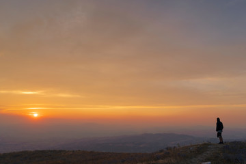 Silhouette of man watching the sunset from the top of a mountain