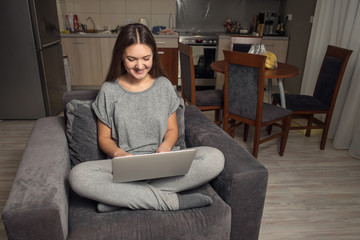 Obraz premium young woman communicates in social networks with laptop, girl sitting at home in chair with laptop