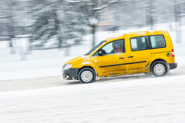 Driving in snow. Motion in blur yellow car in heavy snowfall in city road. Abstract blur winter weather background