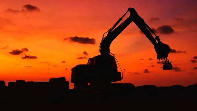 Construction Video At construction site The silhouette excavator is digging ground and lifting a large mortar, with engineering and construction workers to help with colorful sunset .