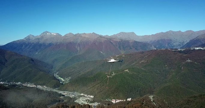 Industrial helicopter flying with load over construction site aerial shooting from drone. Helicopter participates in construction and helps to transport cargo by air in mountain landscape