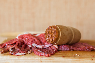 Fresh red meat and a hammer for beating meat. pieces of meat and a kitchen wooden hammer on a wooden background