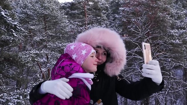 mother and daughter take photo on smartphone in winter forest