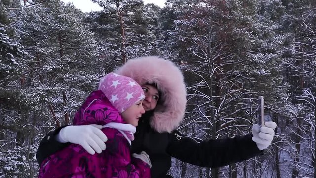 mother and daughter take photo on smartphone in winter forest