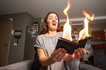 young woman holding a wallet, wallet on fire, surprised girl, magic concept focus, wallet is burning fire